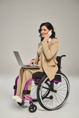 cheerful woman with mobility disability in wheel chair with her laptop and talking by phone clipart