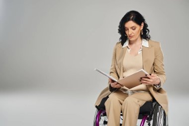 Özürlü, kendine güvenen güzel bir kadın tekerlekli sandalyede otururken evraklarına bakıyor.