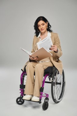 good looking disabled woman in pastel elegant suit working on her paperwork while in wheelchair clipart