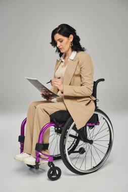Zarif giyimli engelli kadın tekerlekli sandalyede oturuyor ve grafikleri üzerinde çalışıyor.