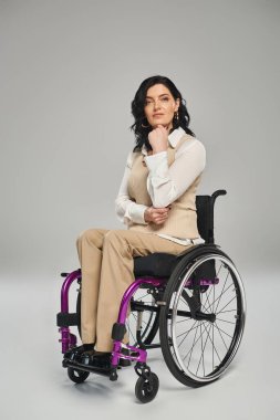 Pastel elbiseli, tekerlekli sandalyede oturan ve kameraya bakan kendine güvenen güzel bir engelli kadın.