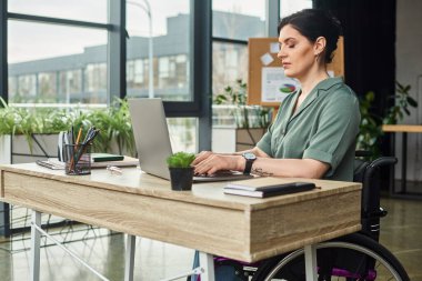 Tekerlekli sandalyede sakat ve kendine güveni tam bir kadın ofiste laptopuyla çok çalışıyor.