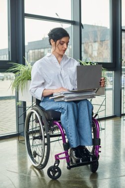 Tekerlekli sandalyede dizüstü bilgisayara bakarak hareket engelli çekici bir iş kadını.