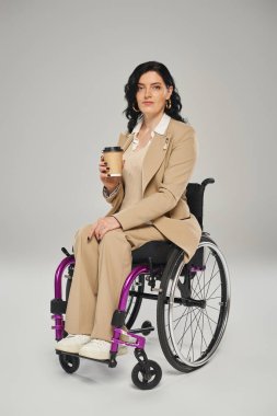 attractive disabled woman in pastel attire in wheelchair holding coffee and looking at camera clipart