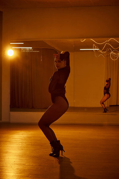 A poised dancer in fishnet tights and black leotard performing dance in a studio