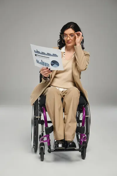 stock image attractive brunette woman with disability with glasses working on graphics while in wheelchair