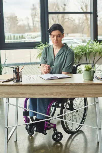 beautiful confident businesswoman in casual attire in wheelchair working with her notebook in office