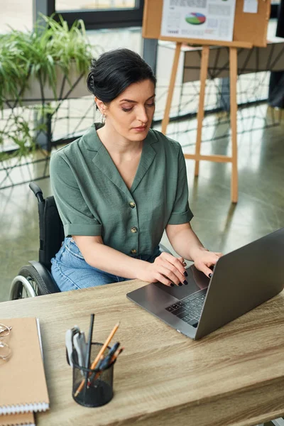 good looking businesswoman in casual attire in wheelchair working at her laptop while in office