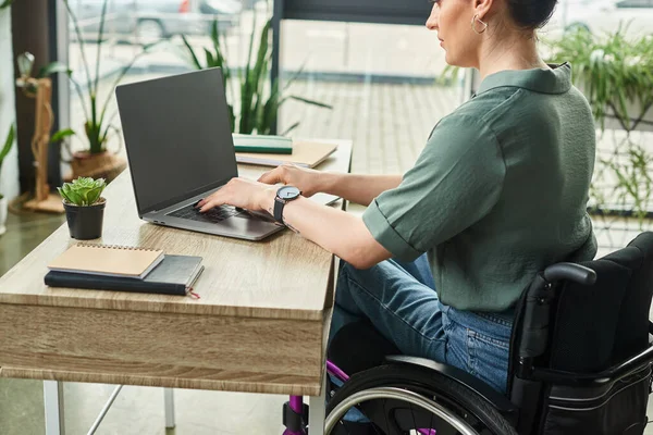 attractive disabled businesswoman in casual attire in wheelchair sitting at laptop working in office