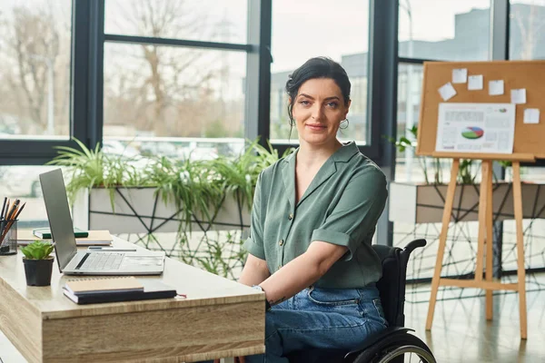 cheerful attractive woman with disability in her wheelchair looking at camera during work in office