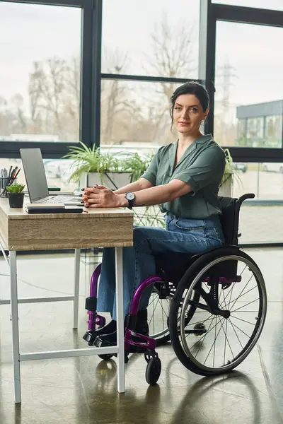 joyous disabled businesswoman in casual attire in wheelchair looking at camera while working hard