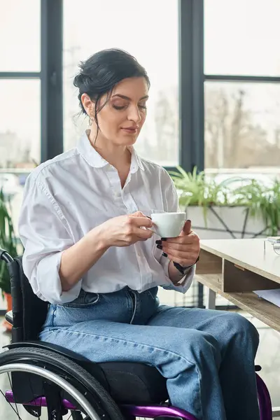 beautiful dedicated woman with mobility disability in wheelchair holding cup of coffee while in office