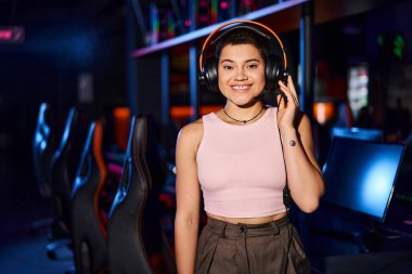 Genç bir kadın siber spor kulübünde kulaklıklarıyla müzik dinlerken neşe saçıyor.