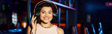 A young woman radiates joy as she listens to music through her headphones in cybersport club, banner clipart