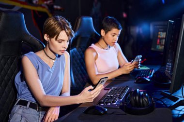 Bilgisayar masasında oturan iki genç kadın siber spor oyun kulübünde telefonlarını kaydırıyor.