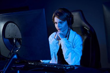 mavi ışıklı bir odada bilgisayara bakan kısa saçlı kadın, siber spor ve oyun konsepti