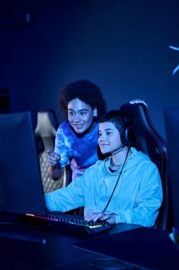 smiling interracial women focused on a cybersport gaming session, female friends looking at monitor clipart