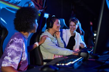 happy interracial women zoomers engaged in cybersport games, using computers and headphones clipart