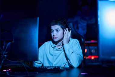 focused young gamer looking at computer monitor while playing game in a blue lit room, cybersport clipart
