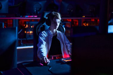 Kulaklıklı genç oyuncu oyun stratejisi ve siber spor hakkında düşünürken bilgisayar monitörüne bakıyor.