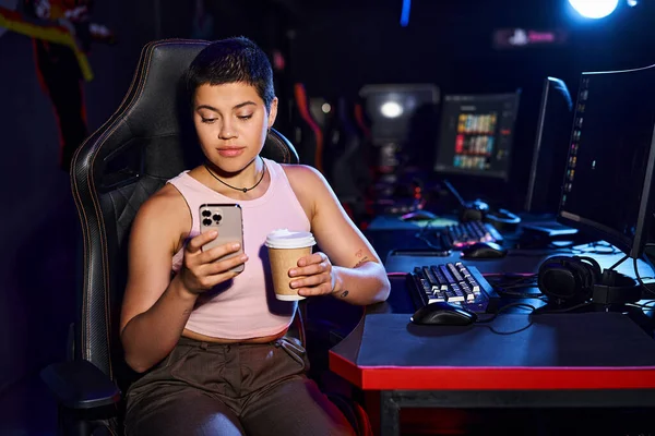 stock image young stylish woman sitting at a desk with a phone in hands and a cup of coffee, Cybersport games