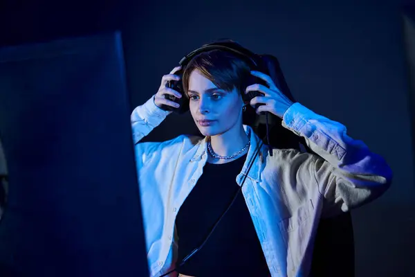 Stock image focused woman wearing headphones and looking at computer in a blue-lit room, cybersport game concept