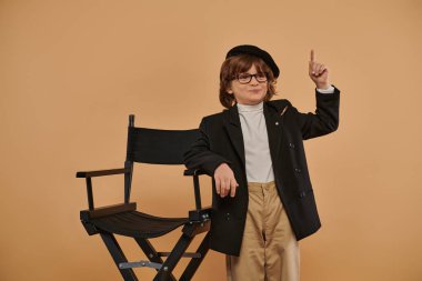 happy boy standing near director chair, with a smile on face showing idea sign,  profession clipart