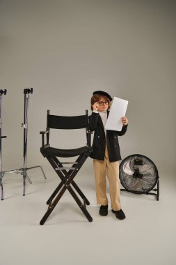 Gözlüklü ve bereli şık bir çocuk, film yapımcısı olarak çocuk, gri üzerine kağıt üzerinde senaryo okuyor.