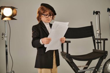 well-dressed kid in glasses and beret holding screenplay on papers, boy as director of filmmaker clipart