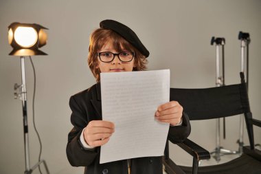 well-dressed kid in glasses and beret reading screenplay on papers, boy as director of filmmaker clipart