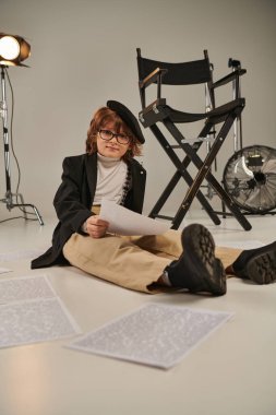 kid in glasses and beret reading screenplay and sitting on floor, boy as director of filmmaker clipart