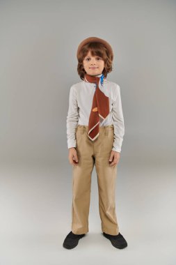Beyaz gömlekli ve gri pantolonlu, şık giyinen, rahat bereli ve eşarplı çocuk.