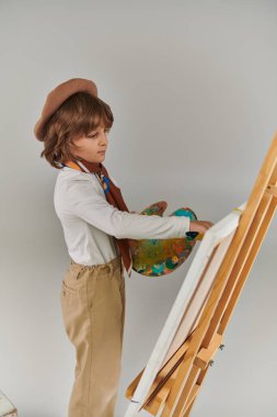 Şövalenin yanında renkli paletli genç bir sanatçı, bereli ve meslekli şık bir çocuk.