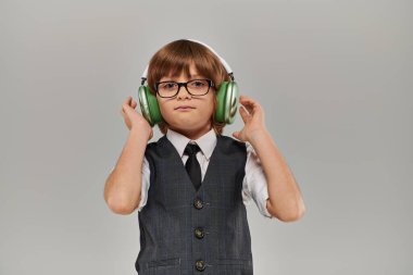Gözlüklü şık bir çocuk ve kulaklıklarıyla müzik dinleyen bir yeleği var.