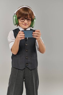 Gözlüklü şık çocuk ve şık giyinmiş kulaklıklı müzik dinliyor ve mobil oyun oynuyor.