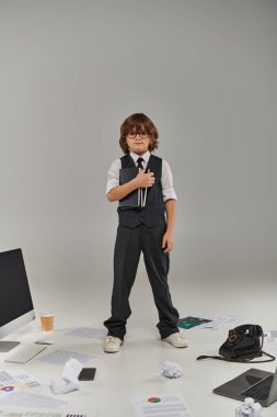 A young professional surrounded by technology and office supplies, holding notebooks on grey clipart