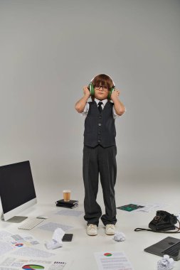 boy immerses himself in digital world, kid in headphones standing near devices and papers on floor clipart