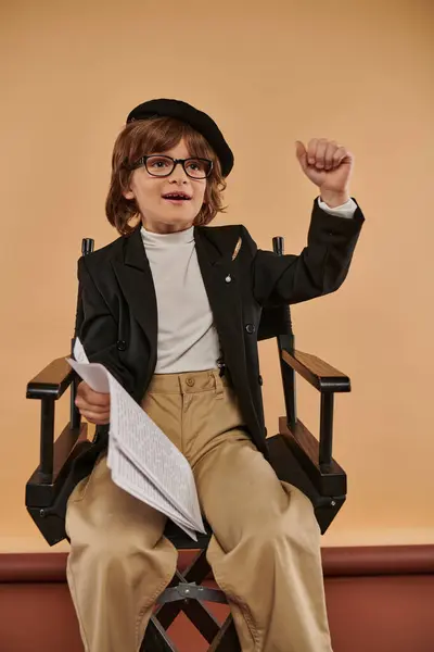 determined boy sits in director chair with papers in hands, ready to conquer the world as film maker