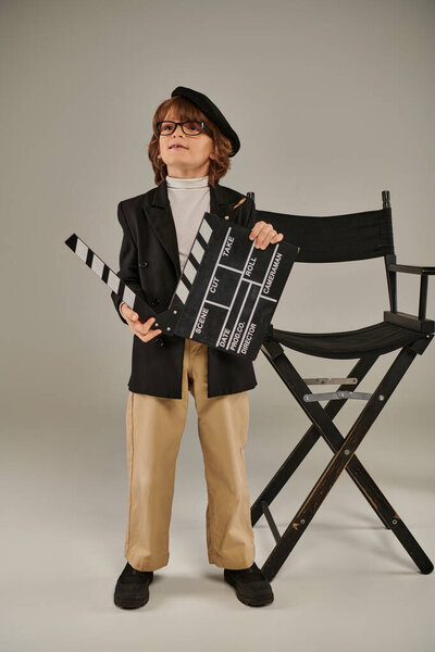 стильный режиссер в беретах и очках, держащий доску объявлений и стоящий рядом с режиссерским креслом