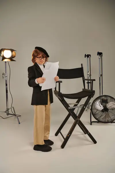 stock image well-dressed boy in glasses and beret holding screenplay on papers, kid as director of filmmaker