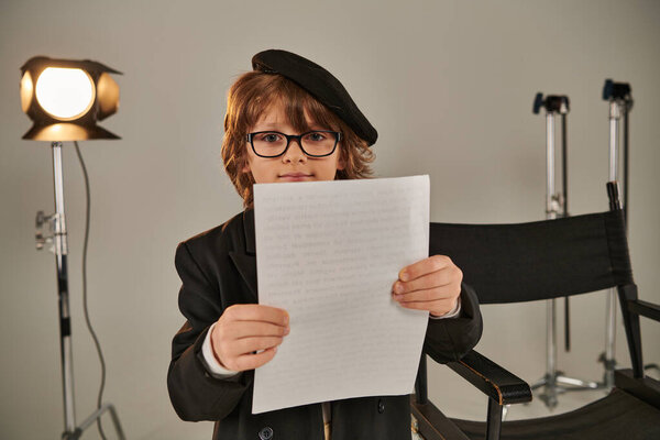 well-dressed kid in glasses and beret reading screenplay on papers, boy as director of filmmaker