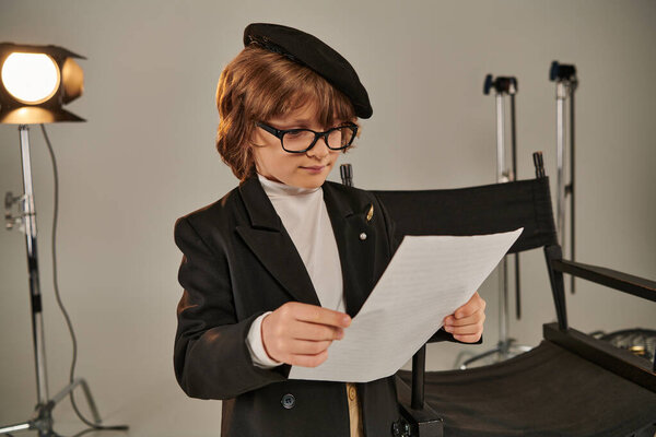 stylish kid in glasses and beret reading screenplay on papers, boy as director of filmmaker