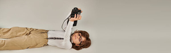 happy kid captures a moment while lying on floor, boy in beret and glasses with retro camera, banner