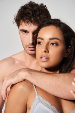 Seksi ve üstsüz adam gri arka planda baştan çıkarıcı genç ve güzel kadına sarılıyor.