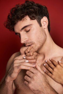 İyi görünümlü ve gömleksiz bir adam kız arkadaşının elini öpüyor. Kırmızı arka planda.