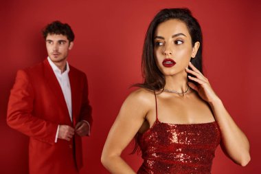 Kırmızı arka planda bulanık adamın yanında parlak rujlu muhteşem ve genç bir kadına odaklan.