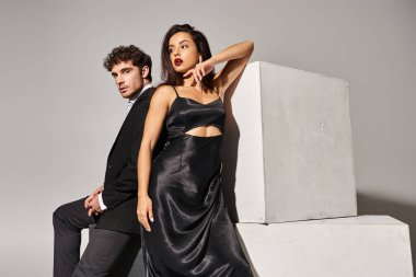 Zarif akşam elbiselerindeki çekici genç çift gri arka planda küplerin yanında poz veriyorlar.