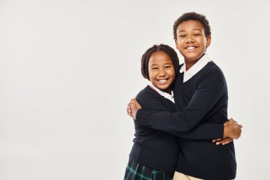 Üniformalı Afro-Amerikan okul çocukları gri arka planda birbirlerine sarılıyorlar.