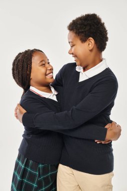 Okul üniformalı Afro-Amerikan çocuklar gri arka planda birbirlerine sarılıyorlar.