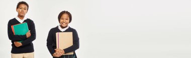 Güzel üniformalı Afro-Amerikan öğrencileri ellerinde kitaplarla gri pankartın üzerinde duruyorlar.